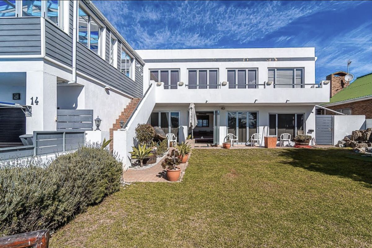 Rear view of the property featuring a landscaped garden, paved patio area, balcony, and multiple sliding glass doors providing access to the interior.