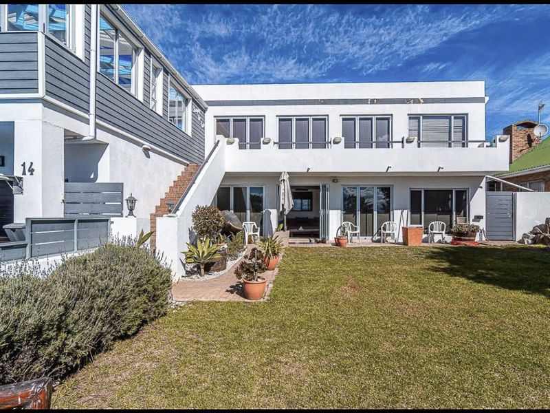 Rear view of the property featuring a landscaped garden, paved patio area, balcony, and multiple sliding glass doors providing access to the interior.