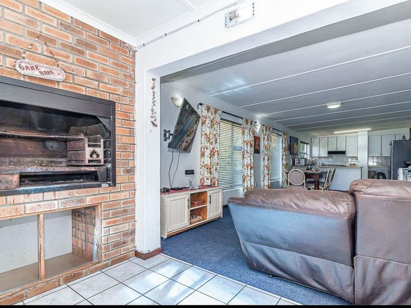 Open-plan living area featuring a built-in brick fireplace, tiled and carpeted flooring, and an adjoining kitchen with functional cabinetry.