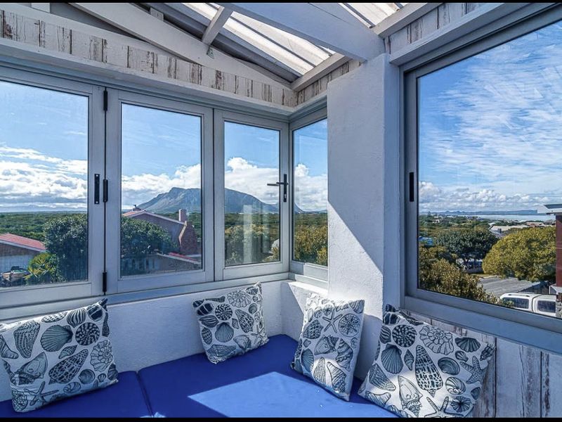 A bright, enclosed balcony featuring expansive windows with panoramic mountain and landscape views, finished with timber cladding and a translucent roof.