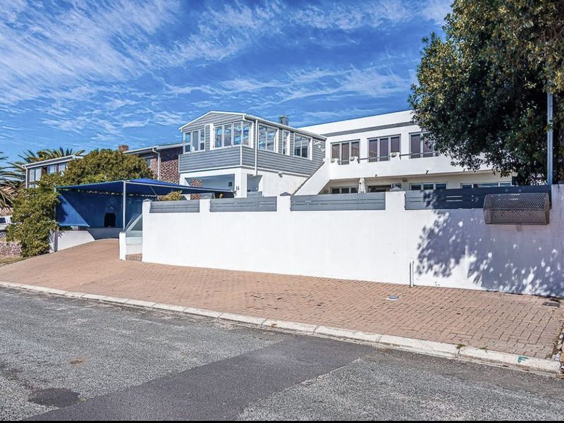 Front exterior view of a multi-level residential property featuring a paved driveway, carport, boundary wall, and upper-level balcony.