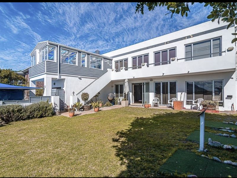 Rear view of a two-story house featuring a lawn, paved patio area, balcony, and external staircase access.