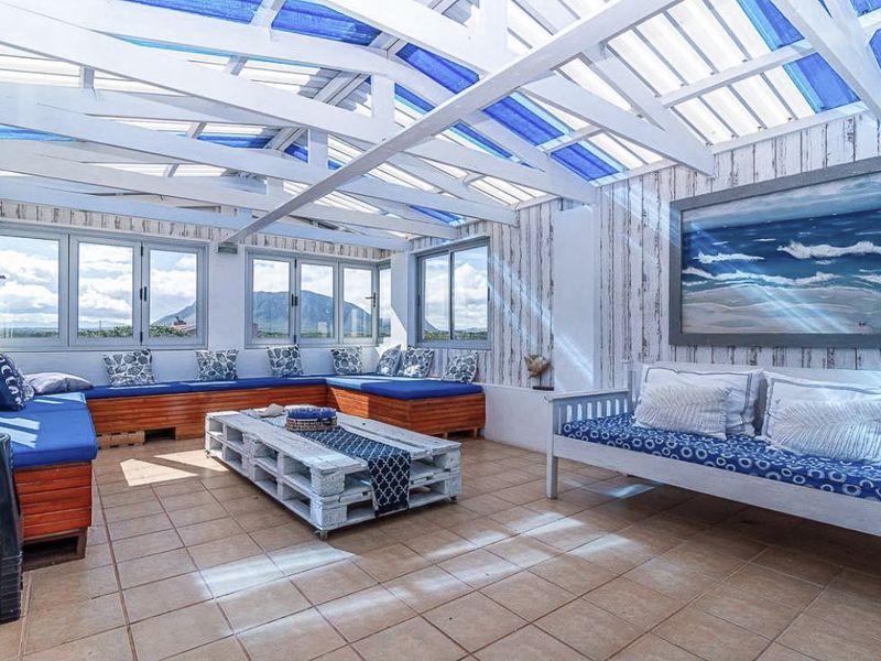 A bright, covered patio area featuring tiled flooring, a timber-framed translucent roof, and expansive windows offering scenic mountain views.