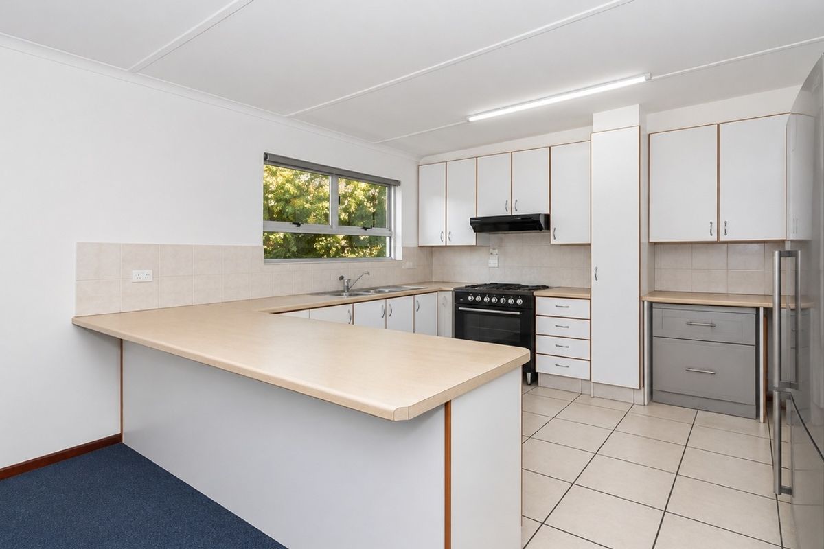 A functional kitchen featuring laminate countertops, built-in cabinetry, a gas stove with extractor fan, and tiled flooring, offering a clean and practical workspace.