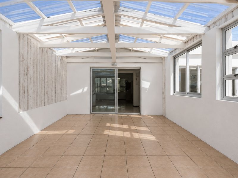 A bright, enclosed patio area featuring a translucent roof, tiled flooring, and sliding glass doors leading into the main living space.