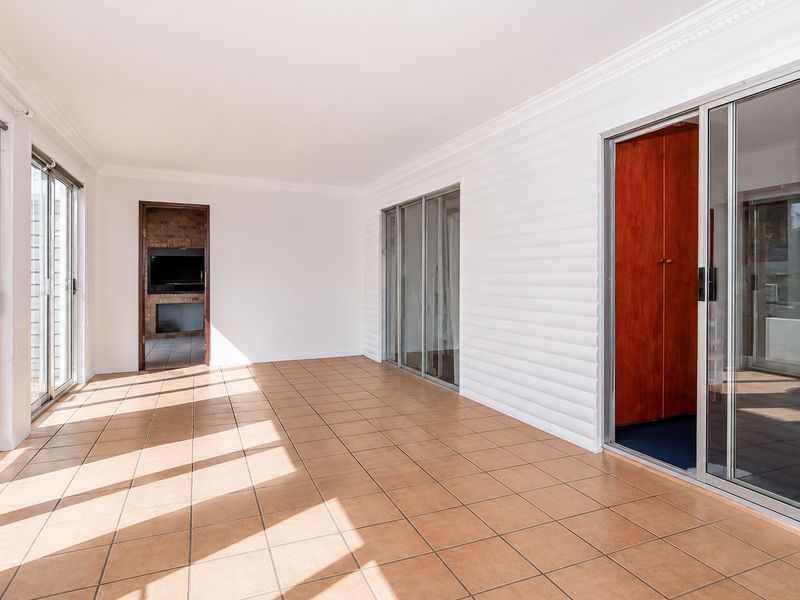 A bright, enclosed patio area featuring tiled flooring, sliding glass doors, and a built-in fireplace, offering a versatile space for indoor-outdoor living.