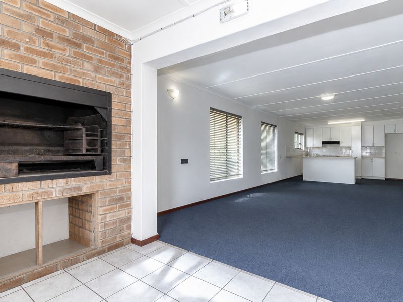 Spacious open-plan living area featuring a built-in brick fireplace, tiled and carpeted flooring, and a functional kitchen with ample cabinetry.