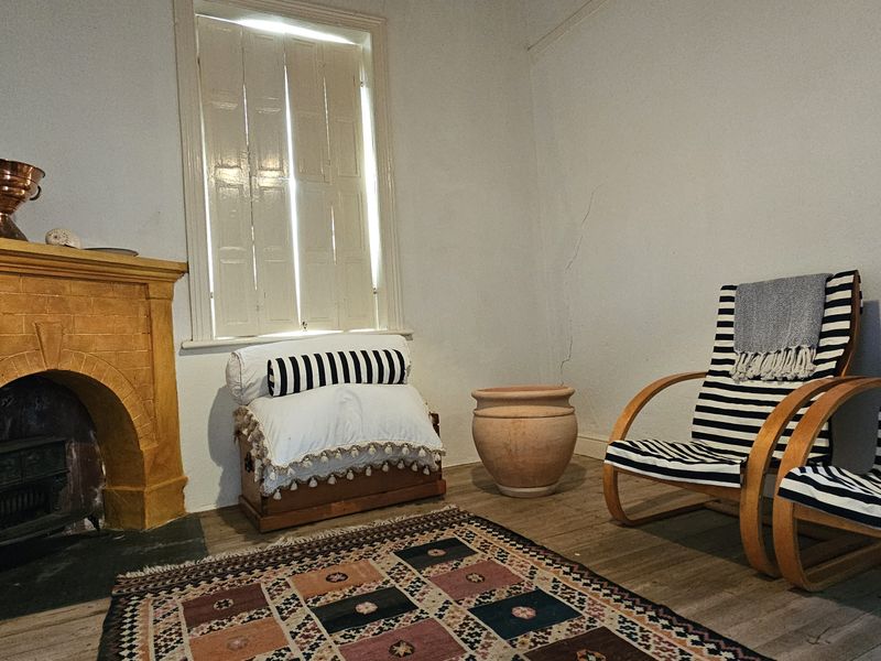A living room featuring a rustic brick fireplace, timber flooring, and traditional window shutters, showing signs of wear including visible wall cracks.