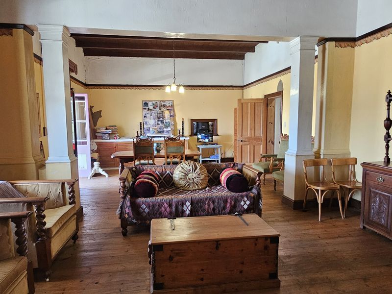 Spacious open-plan living and dining area featuring original hardwood flooring, exposed timber ceiling beams, and classic architectural columns.