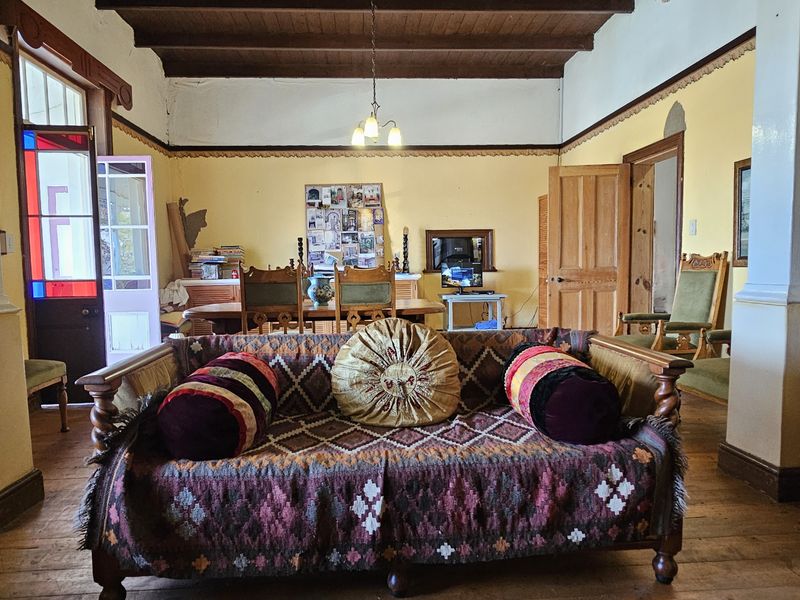 Spacious living area featuring exposed timber ceiling beams, original timber flooring, and a characterful stained glass door leading to the exterior.