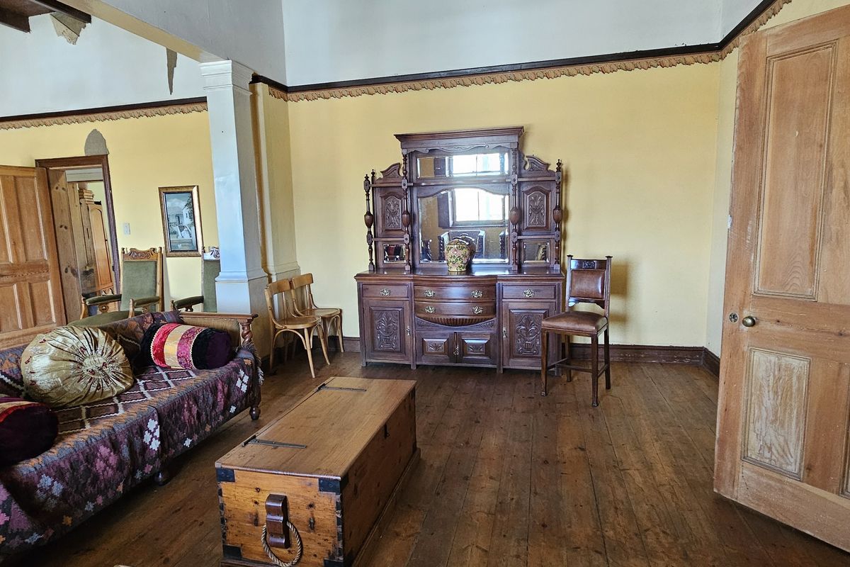 Spacious living area featuring original timber flooring, classic timber doors, and decorative cornicing, requiring some ceiling repairs and cosmetic updates.