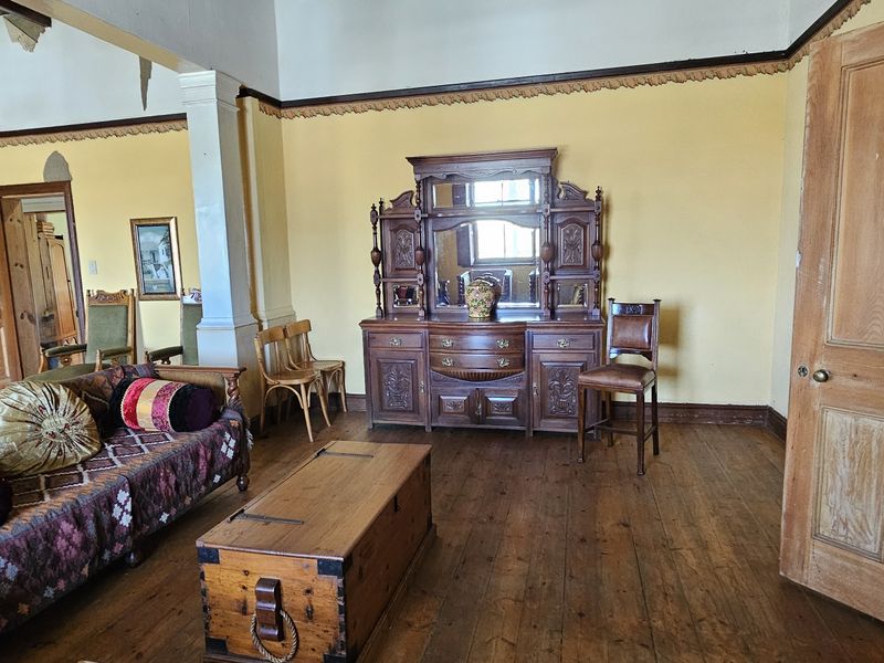 Spacious living area featuring original timber flooring, classic timber doors, and decorative cornicing, requiring some ceiling repairs and cosmetic updates.