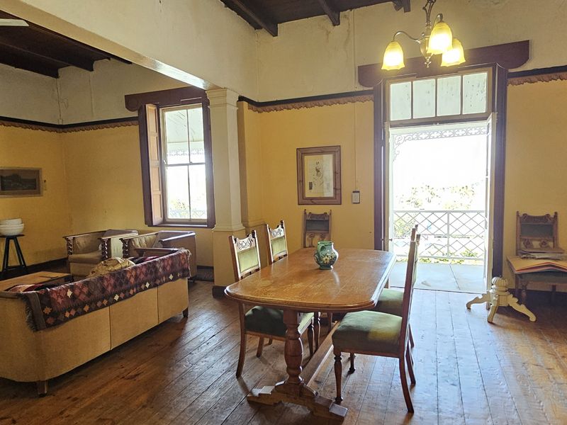 Spacious open-plan living and dining area featuring original timber flooring, exposed ceiling beams, and direct access to a balcony through classic french doors.