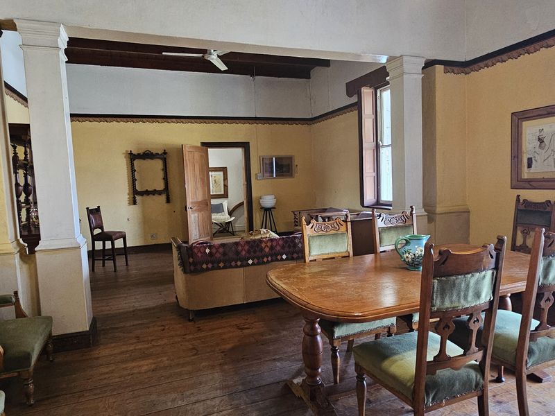 Spacious open-plan living and dining area featuring original hardwood flooring, decorative cornicing, and structural columns, offering a classic character aesthetic.