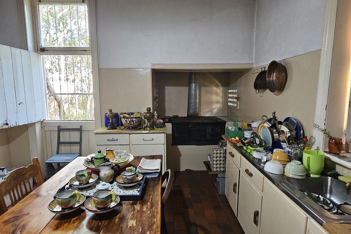 A rustic kitchen featuring vintage cabinetry, a traditional wood-burning stove, and a stainless steel sink, offering significant potential for a modern renovation.