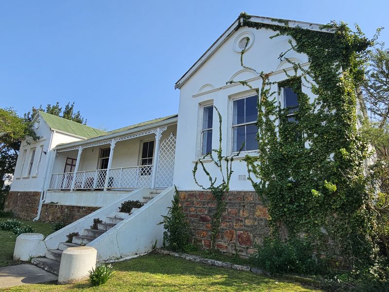 A historic-style house featuring a stone masonry base, a raised veranda with wrought iron detailing, and classic sash windows set in a garden.