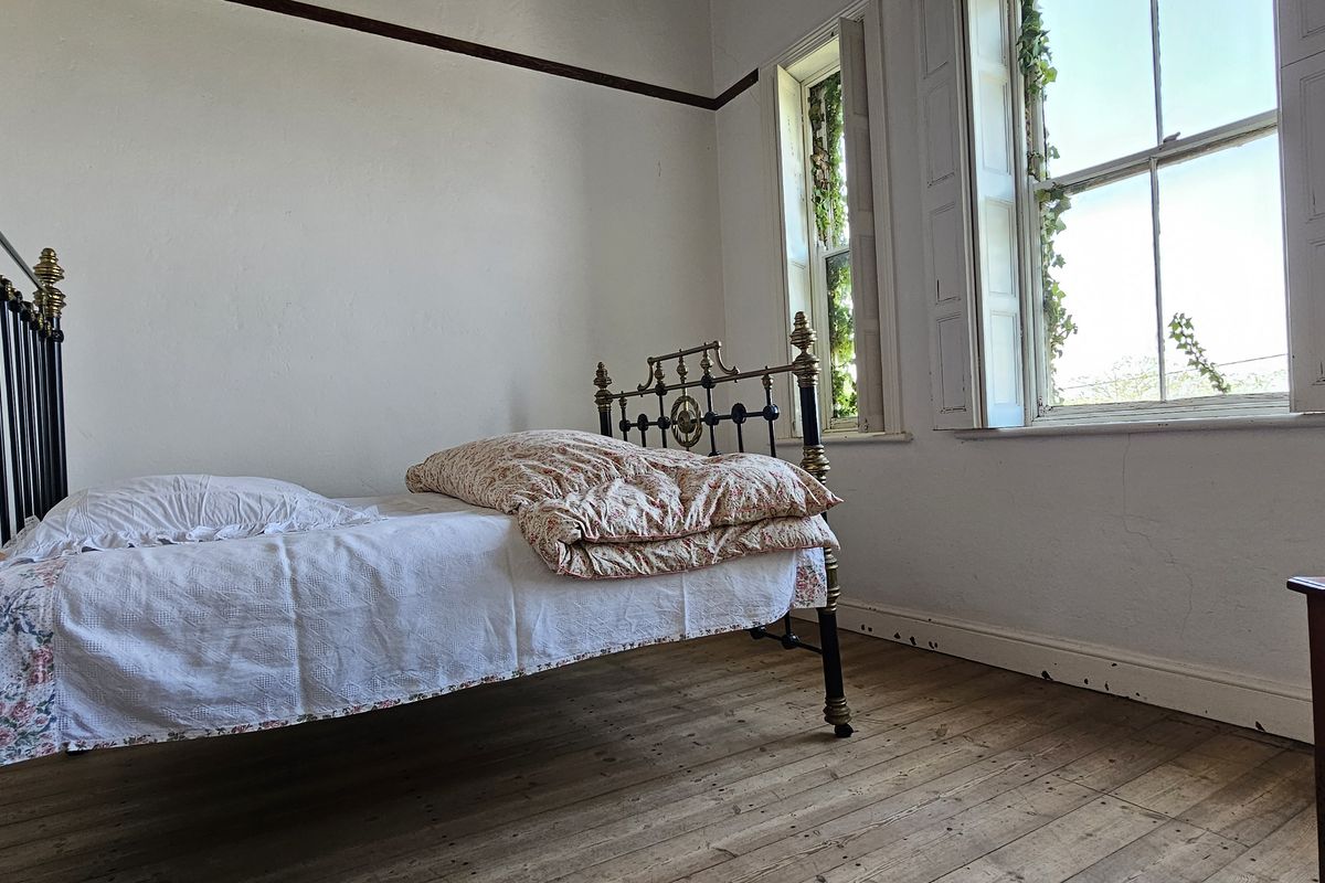 A bedroom featuring original timber flooring, sash windows with shutters, and a picture rail, requiring some cosmetic attention to the walls and skirting.