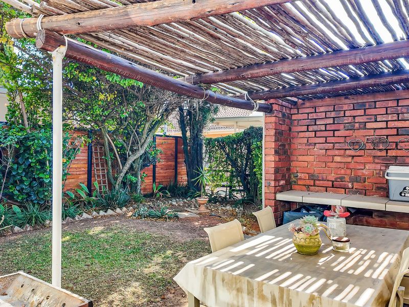 Covered outdoor patio area featuring a rustic timber pergola, exposed brick wall, and a built-in concrete counter, overlooking a private garden space.