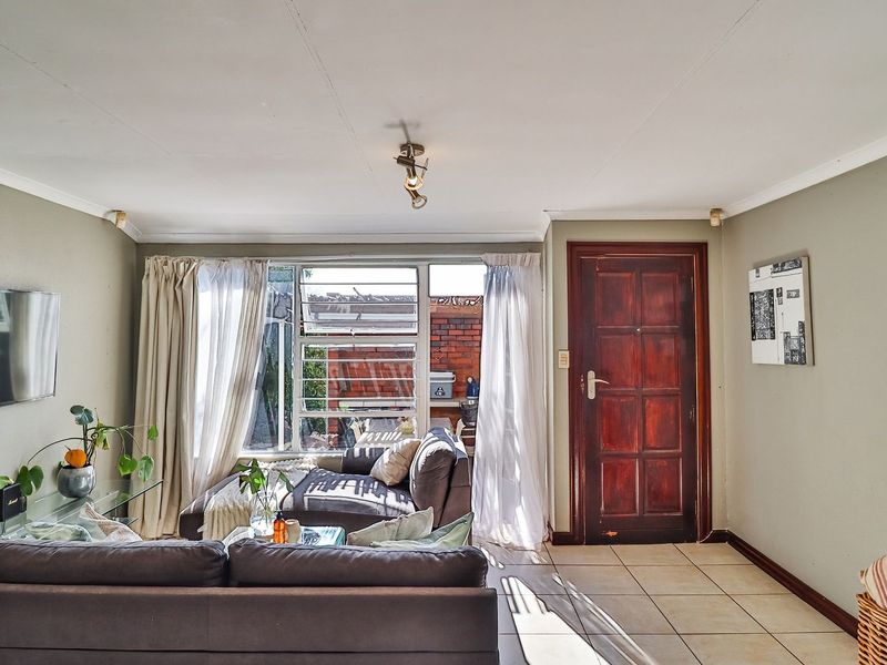 A living room featuring tiled flooring, a timber entrance door, and large windows with security bars, offering a functional and well-lit living space.