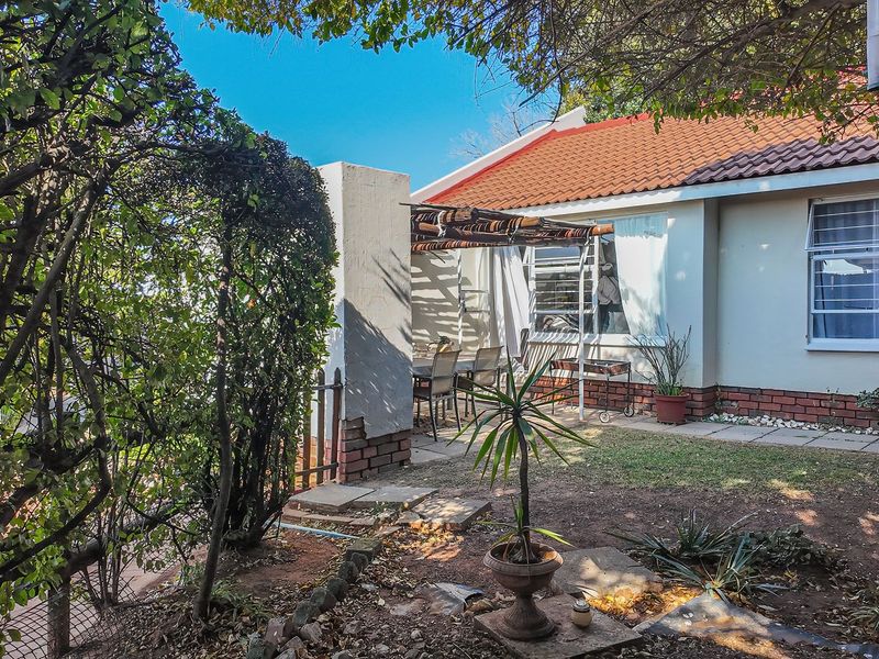 Rear view of the townhouse featuring a paved patio area, pergola, and established garden with a tiled roof and brick foundation.