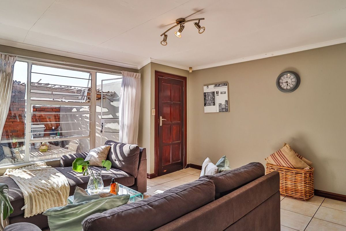 A bright living room featuring tiled flooring, a timber entrance door, and large windows providing natural light and access to the outdoor area.