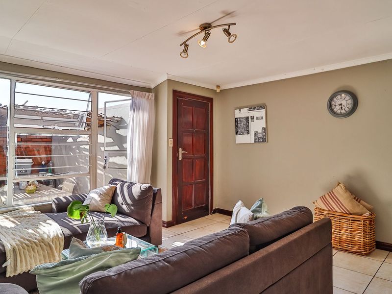 A bright living room featuring tiled flooring, a timber entrance door, and large windows providing natural light and access to the outdoor area.