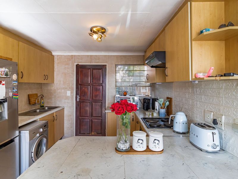 Functional kitchen featuring built-in cabinetry, laminate countertops, electric hob, extractor fan, and tiled backsplash with direct access to an exterior door.