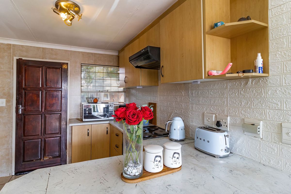 A functional kitchen featuring light wood cabinetry, a tiled backsplash, and a built-in electric hob with an extractor fan.