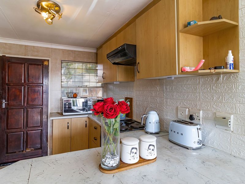 A functional kitchen featuring light wood cabinetry, a tiled backsplash, and a built-in electric hob with an extractor fan.