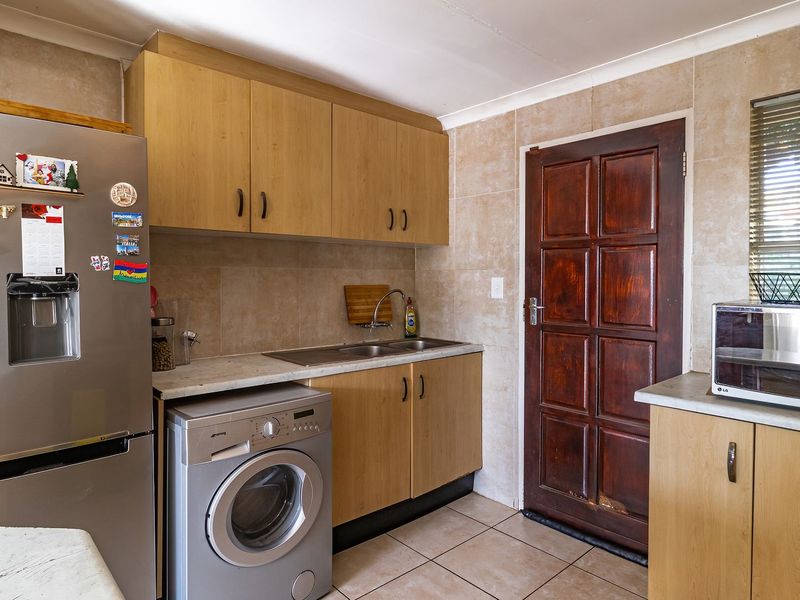 Functional kitchen featuring laminate cabinetry, tiled splashbacks, double bowl sink, and direct access to the exterior via a timber panel door.