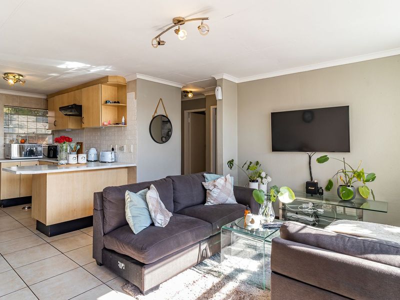 Open-plan living area featuring a functional kitchen with light wood cabinetry and tiled flooring, seamlessly flowing into a comfortable lounge space.