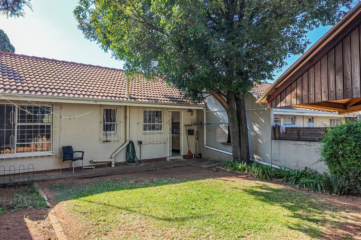 Rear view of the townhouse featuring a small garden, concrete patio area, and a wooden pergola structure.