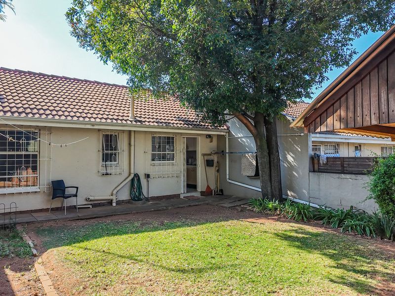 Rear view of the townhouse featuring a small garden, concrete patio area, and a wooden pergola structure.