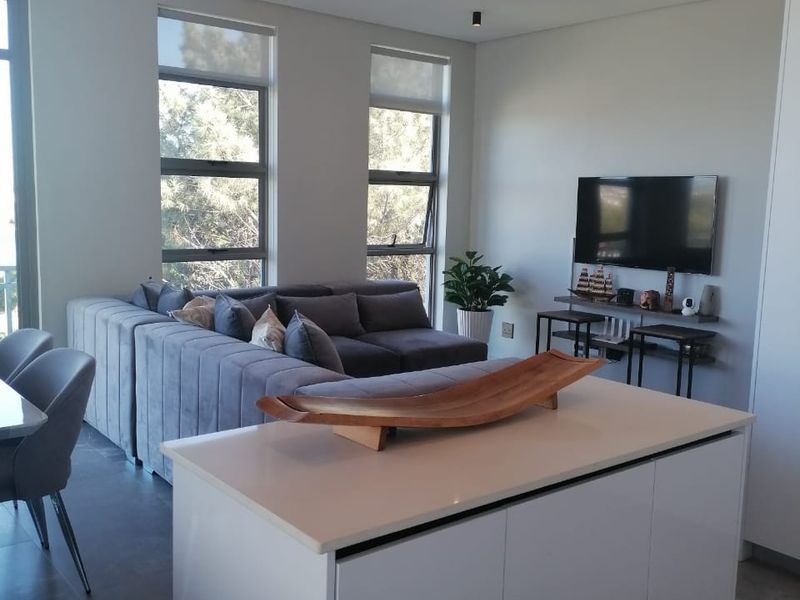 Modern open-plan living area featuring a sleek kitchen island with stone countertop, contemporary lighting fixtures, and large windows providing ample natural light.