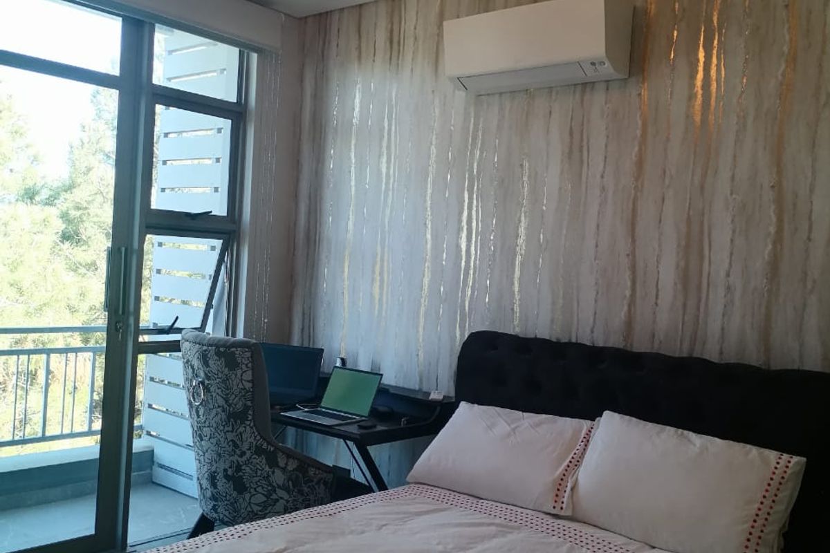 A well-lit bedroom featuring a modern air conditioning unit, textured feature wall, and large sliding glass doors providing access to a balcony.