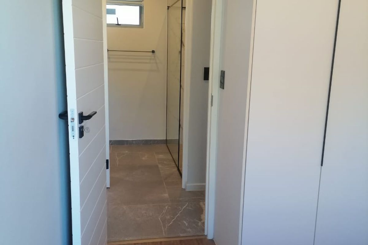 A view from a bedroom into an ensuite bathroom featuring modern tiled flooring, a glass shower screen, and a built-in wardrobe.