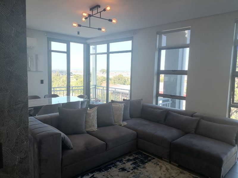 Bright open-plan living and dining area featuring large windows, modern lighting, and direct access to a balcony with scenic views.
