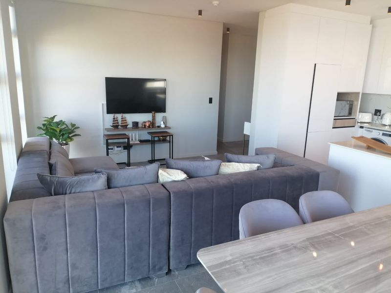 Modern open-plan living area featuring a sleek kitchen with integrated cabinetry, stone countertops, and recessed ceiling lighting, flowing into a comfortable lounge space.