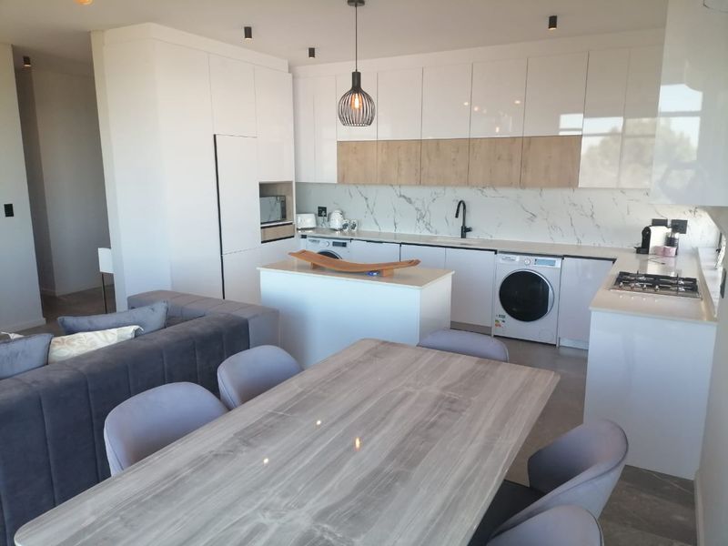 Modern open-plan kitchen and living area featuring sleek white cabinetry, stone countertops, marble-look splashback, and integrated appliances in a contemporary apartment setting.