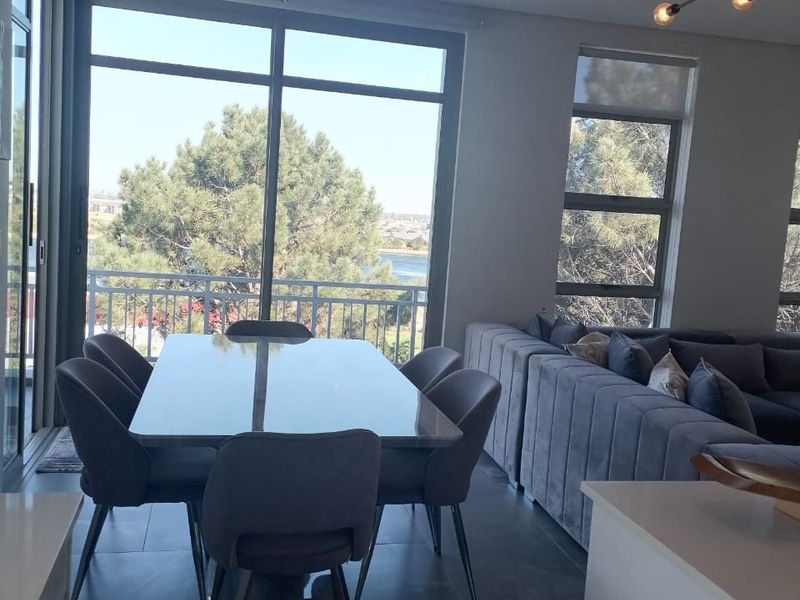 Modern open-plan living and dining area featuring large format floor tiles, expansive windows with natural light, and direct access to a balcony.