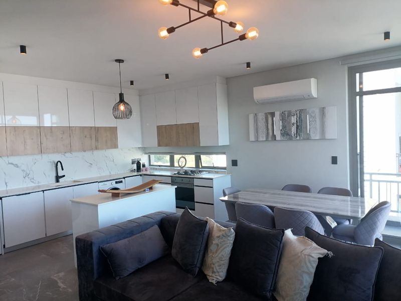 Modern open-plan living area featuring a sleek kitchen with marble-look splashback, integrated appliances, and a spacious dining area leading to a balcony.