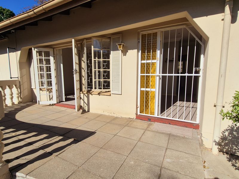 A covered patio area featuring tiled flooring, a decorative balustrade, and secure access points with french doors and security gates.