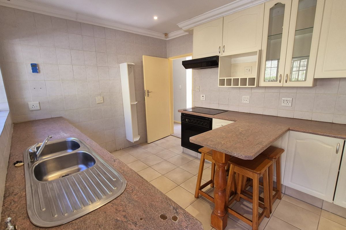 A functional kitchen featuring laminate countertops, double bowl sink, built-in cabinetry, and an electric hob with extractor fan, finished with tiled flooring and splashbacks.
