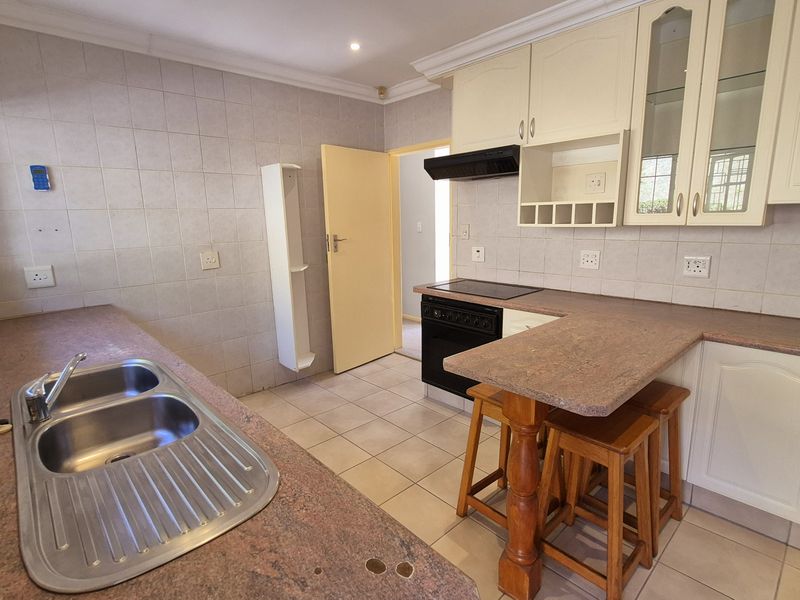 A functional kitchen featuring laminate countertops, double bowl sink, built-in cabinetry, and an electric hob with extractor fan, finished with tiled flooring and splashbacks.
