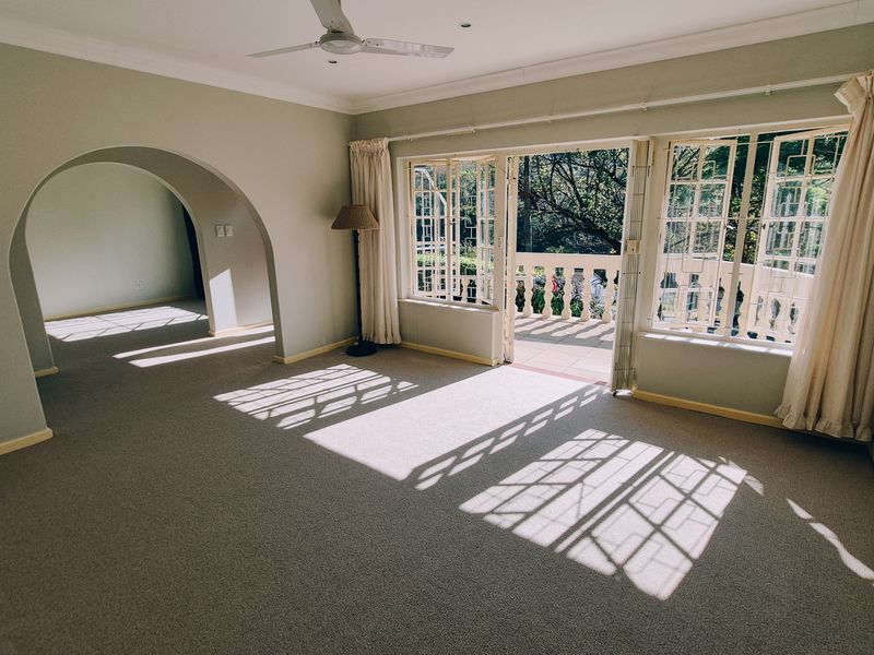 Spacious living room featuring an elegant archway, carpet flooring, and large french doors opening onto a balcony with natural light.