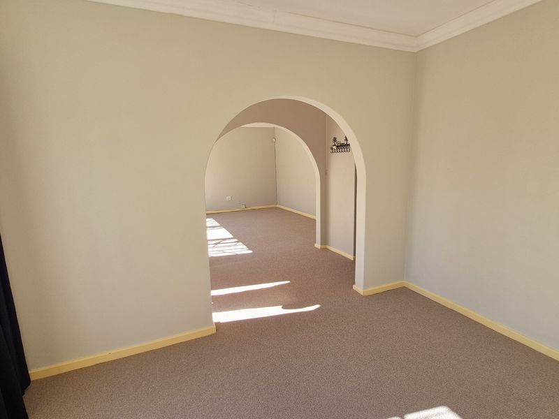An empty living area featuring a distinctive architectural archway connecting to an adjacent room, finished with neutral wall paint and carpeted flooring.