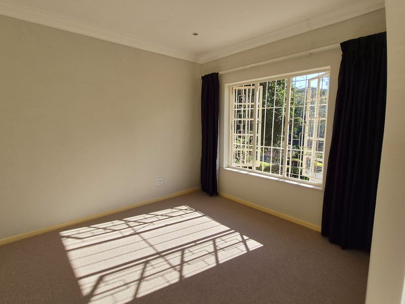 A bright, empty bedroom featuring neutral carpeting, cornice detailing, and large windows fitted with security bars and dark curtains.