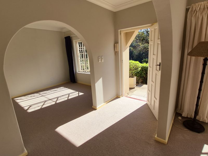 An inviting entrance hall featuring classic arched doorways, neutral carpeting, and natural light, leading directly to an outdoor area.