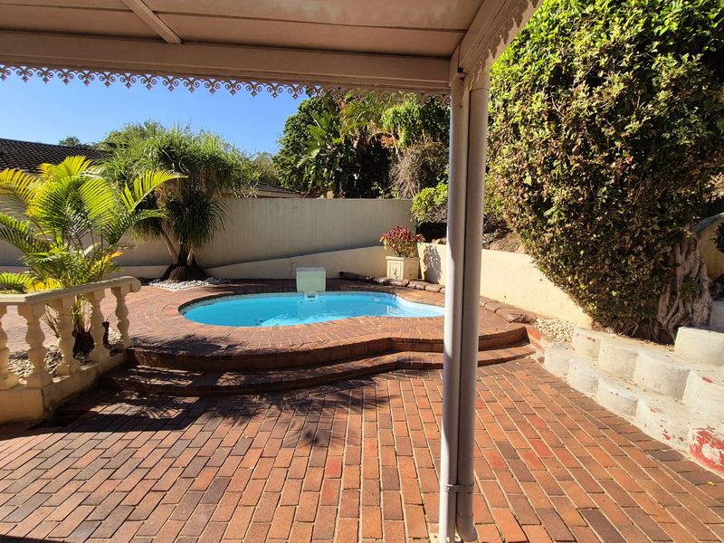 Outdoor pool area featuring a small swimming pool, brick paved patio, and covered veranda space with established garden surroundings.