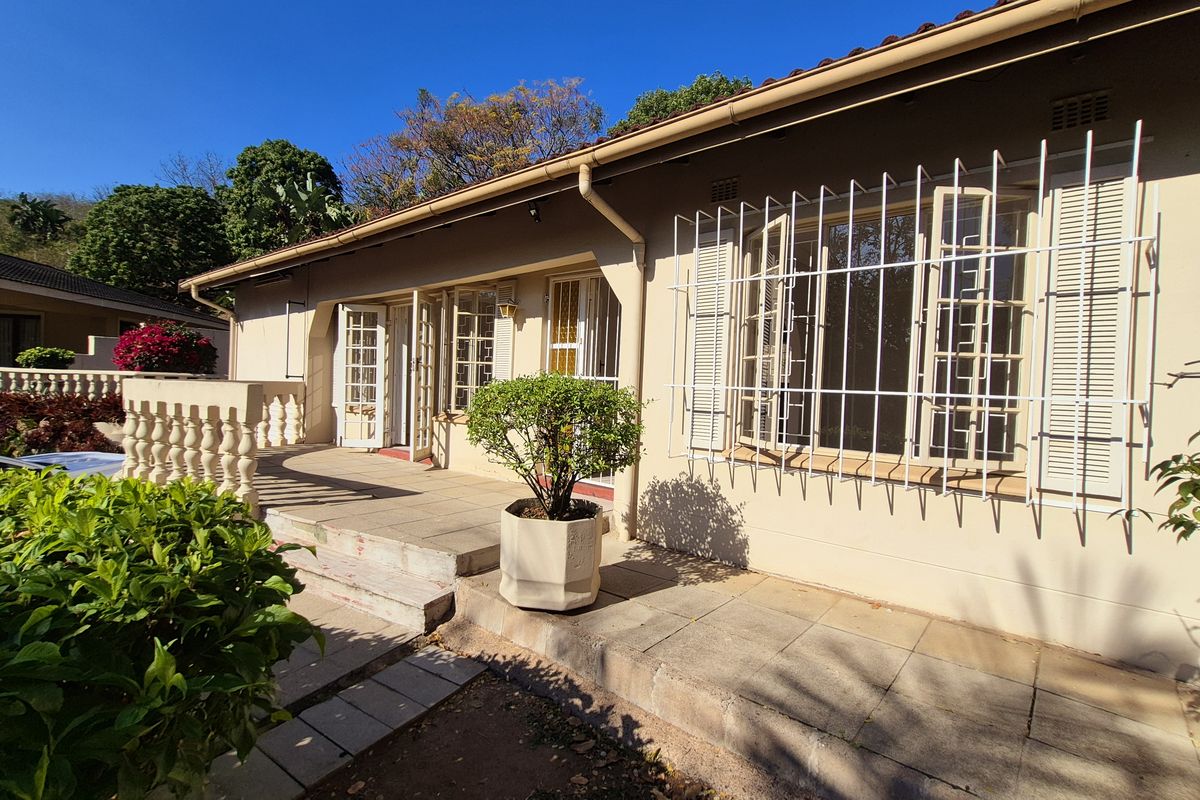 Rear exterior view of the house featuring a tiled patio area, security bars on windows, and a balustrade overlooking the garden.
